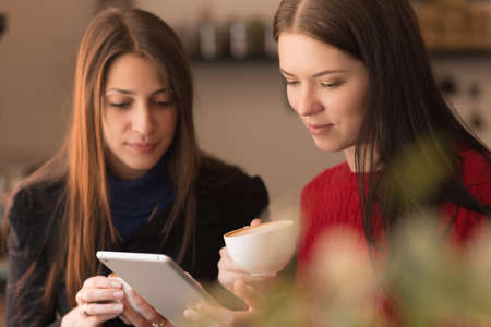 Two girlfriends using tablet and drinking cappuccinoの写真素材