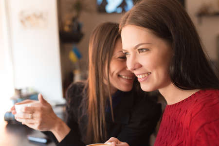 Young funny girlfriends drinking cappuccino in coffee shopの写真素材