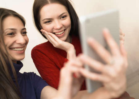 Two girlfriends using tablet in light roomの写真素材