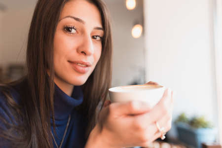 Brunette woman drinking cappuccino in coffee shopの写真素材