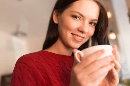 Cute woman in red pullover drinking cappuccino in coffee shopの写真素材