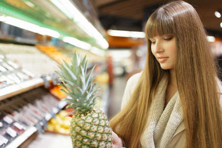 Woman choosing fruits at supermarket and holding pineappleの写真素材