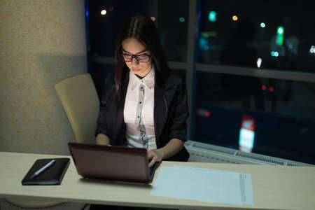 Businesswoman working at a laptop late at night in officeの写真素材