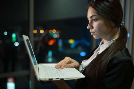 Businesswoman working at a laptop late at night in officeの写真素材