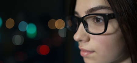 Close-up portrait of a girl with glasses at window late at nightの写真素材