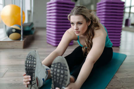 Woman doing stretching exercises on karemat in fitness centerの写真素材
