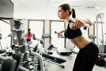 Beautiful woman doing exercise with dumbbell in gymの写真素材