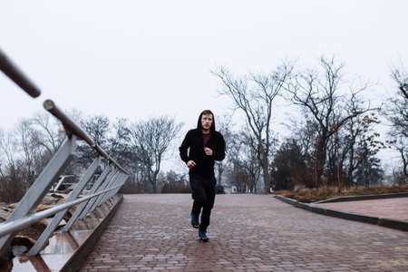 Sporty man jogging through rainy cityscapeの写真素材