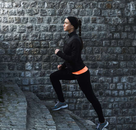 Young athletic woman running up the stairs near brick wallの写真素材