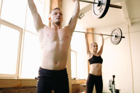 Two people lifting barbells during a gym workout