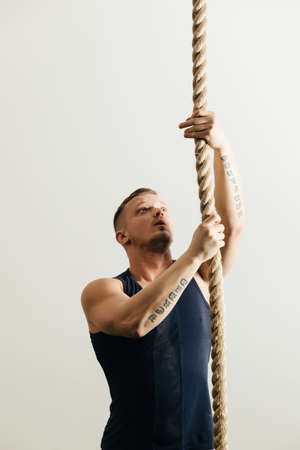 Man climbing rope in gym at white backgroundの写真素材