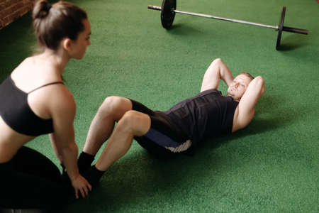 Man doing sit-ups while a young woman steadies her feetの写真素材