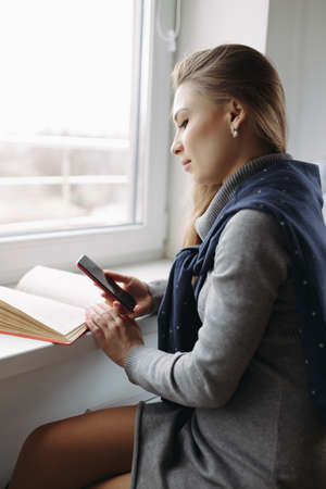 Beautiful young woman using her smartphone at windowの写真素材