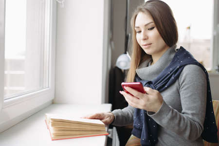 Beautiful young woman using her smartphone at window