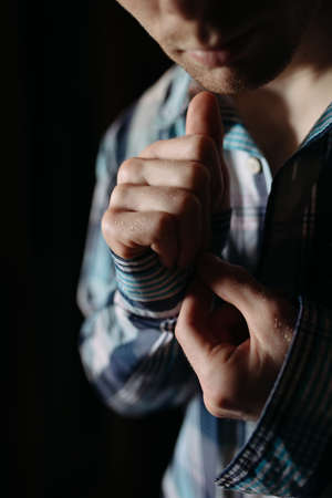 Man buttoning his checkered shirt on black background