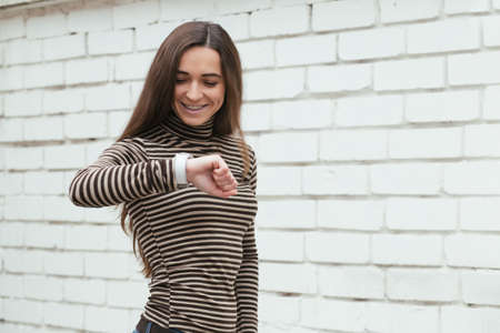 Woman looking at watch against a brick wall backgroundの写真素材