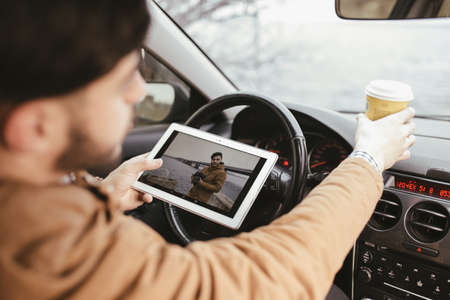 Man holding his digital tablet in car and drinking coffee