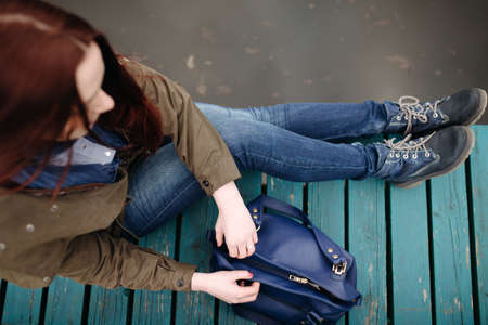 Woman sitting on pier at the river in a cold cloudy day