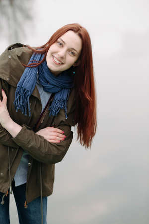 Woman standing on pier at the river in a cold cloudy day and smileの写真素材