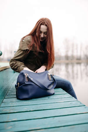 Woman sitting on pier at the river in a cold cloudy dayの写真素材
