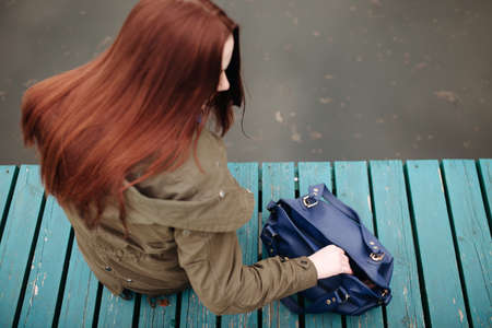 Woman sitting on pier at the river in a cold cloudy dayの写真素材