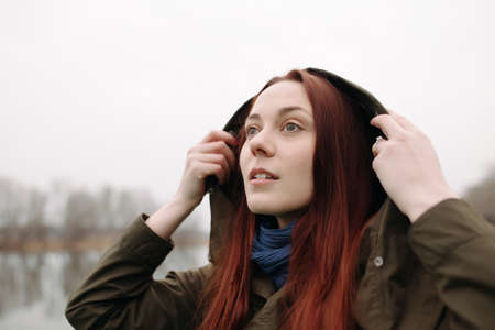 Young woman wearing hood on pier at the riverの写真素材