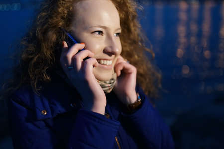 Young happy woman talking by phone in evening city at river quayの写真素材