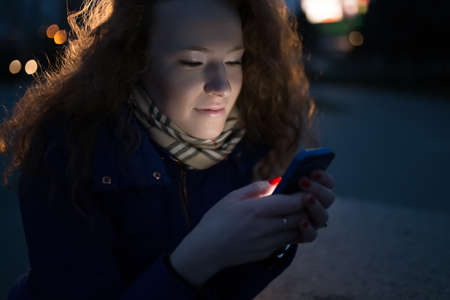 Pretty young woman using her mobile phone in evening cityの写真素材