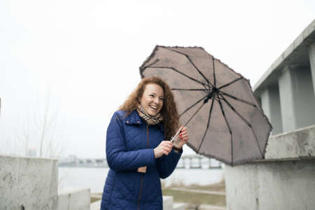 Smiling pretty woman holding umbrella and walking in city