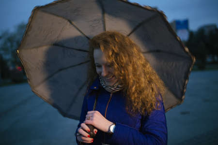 Smiling young woman with umbrella in evening cityの写真素材