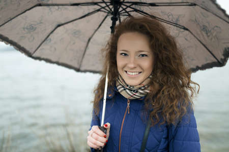 Portrait of young woman with umbrella at river coast on a rainy dayの写真素材