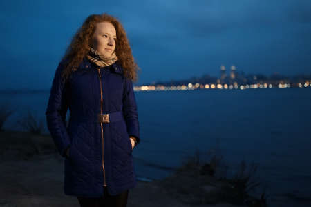 Young woman standing near river coast in city at night timeの写真素材