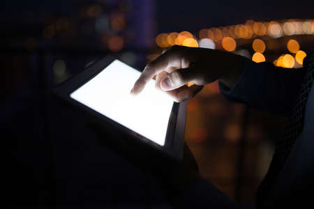 Man's hand holding digital tablet at night city backgroundの写真素材