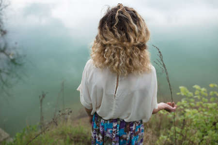 Curly hair woman standing at lake, back viewの写真素材