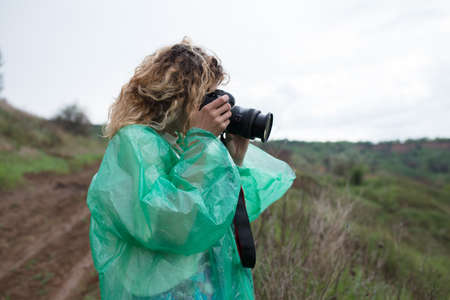 Woman photographer in raincoat take a photo at wildlife landscape