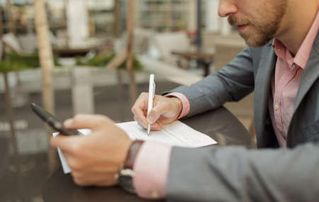 Businessman sitting at outdoor cafe and takes notes. Cropped shot.の写真素材