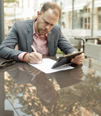 Businessman sitting at outdoor cafe and takes notesの写真素材
