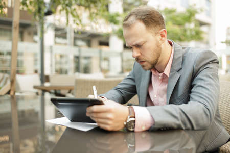 Businessman sitting at outdoor cafe and takes notesの写真素材