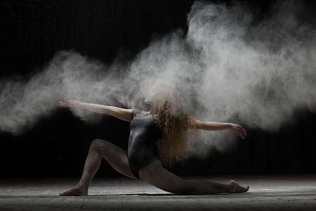 Flexible woman dancing and sprinkle flour on black background