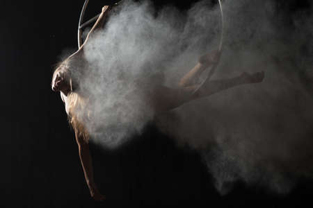 Acrobatic woman doing trick on aerial hoop with sprinkled flourの写真素材