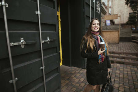 Female customer coming out from cafe with cup of coffee