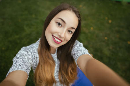 Woman with cute smile make a selfie sitting on grassの写真素材