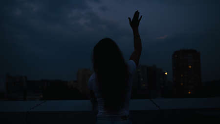 Silhouette of woman make a hand up gesture in dusk cityの写真素材