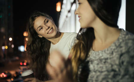 Two young woman friends speaking in balcony at night