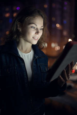 Young women look down to digital tablet in balcony at night cityの写真素材