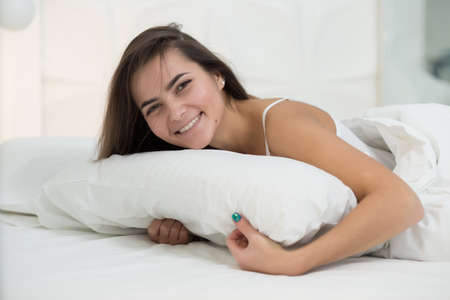 Woman lying on a white bed in home and smile. Good morning.