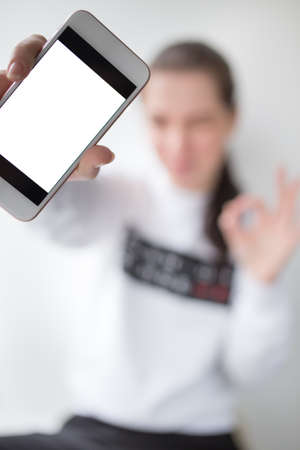 Young woman showing screen on her smartphone against white backgroundの写真素材