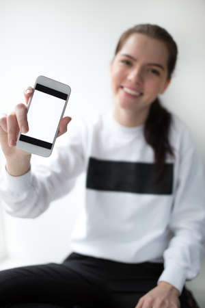 Young woman showing screen on her smartphone against white background
