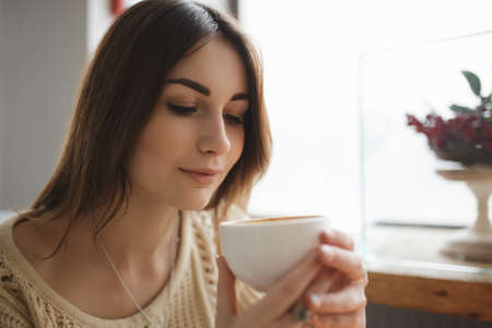 Woman typing text on smartphone in a cafe while coffee is coolsの写真素材