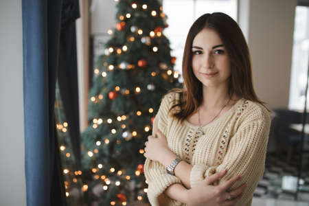 Portrait of lovely woman in pullover at christmas tree backgroundの写真素材